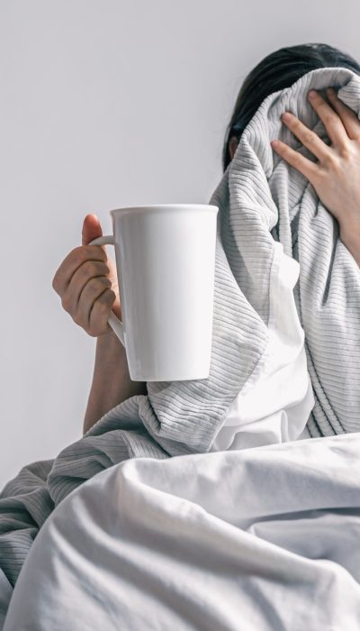 A sleepy young woman holding coffee cup in bed, morning routine concept.